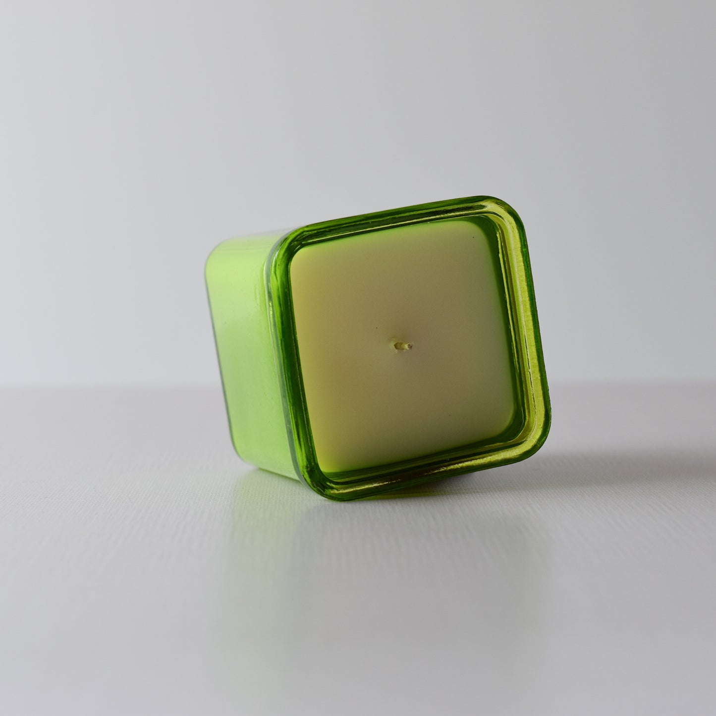 Green glass candle holder with a white candle inside on a light gray background