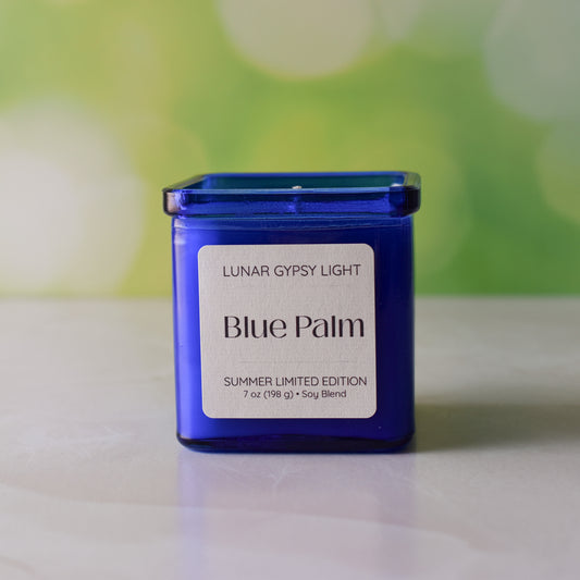 Blue candle labeled 'Blue Palm' by Lunar Gypsy Light on a white surface with a blurred green background