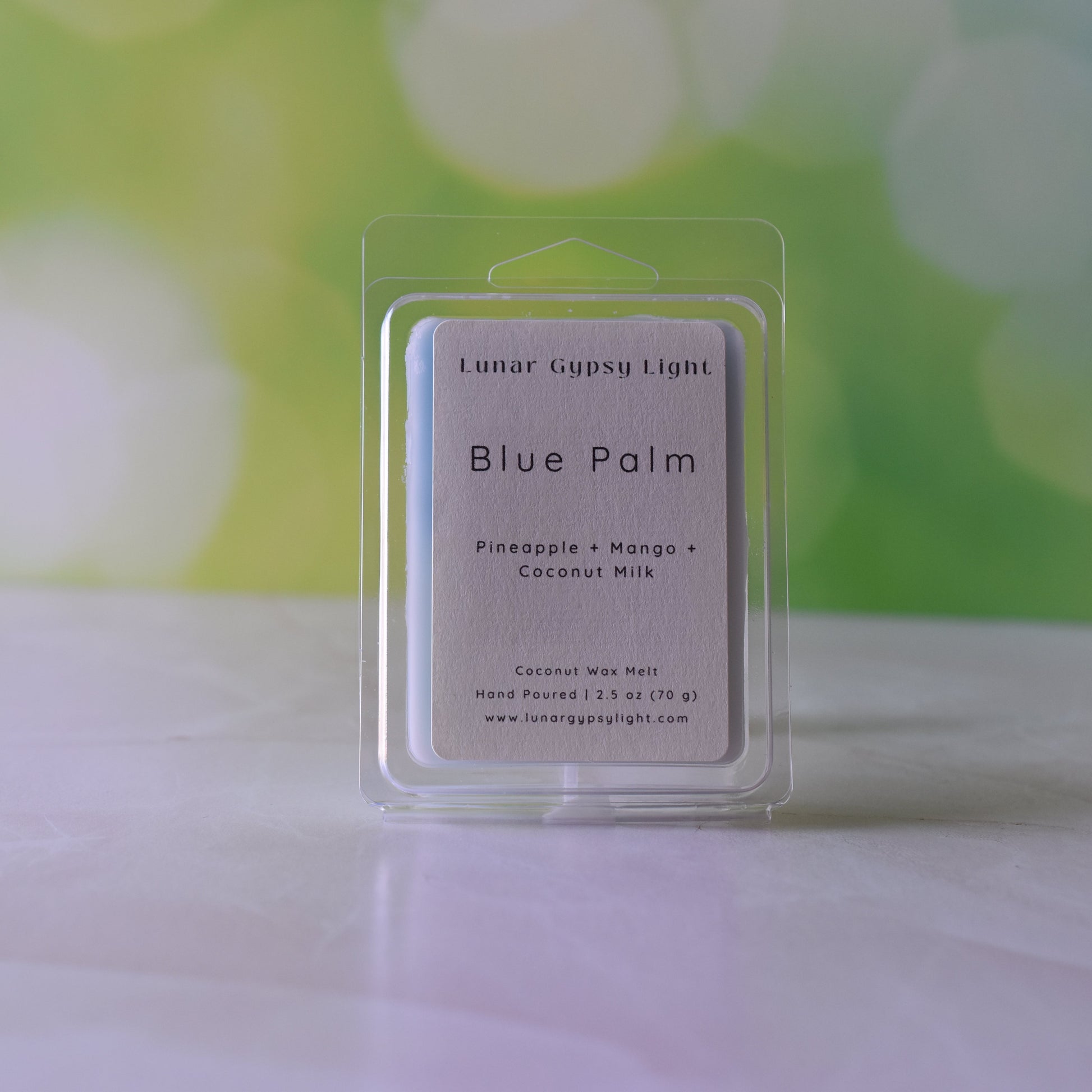 Packaged Wax melt labeled Blue Palm on white surface with green and yellow blurred background