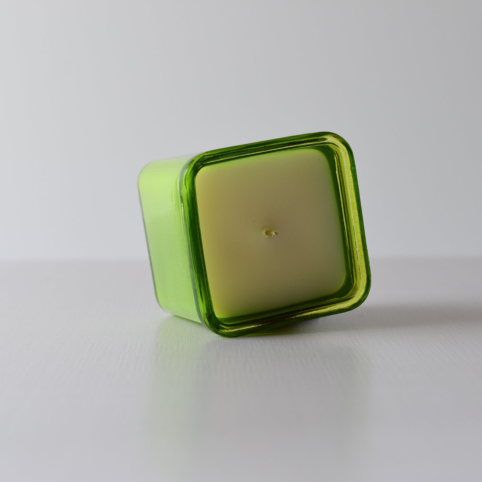 Green glass candle holder with a white candle inside on a light gray background