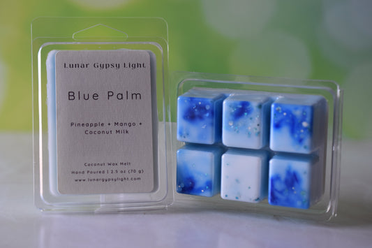 Packaged wax melts with 'Blue Palm' scented with Pineapple Mango and Coconut Milk on a white surface with green and yellow blurred background