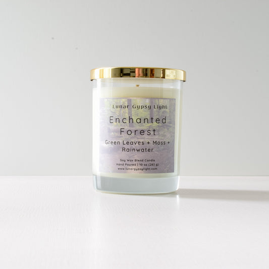 Candle labeled 'Enchanted Forest' with gold lid on a white background