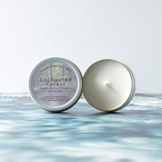 Candle and its packaging labeled 'Enchanted Forest' on a fir inspired surface and white background