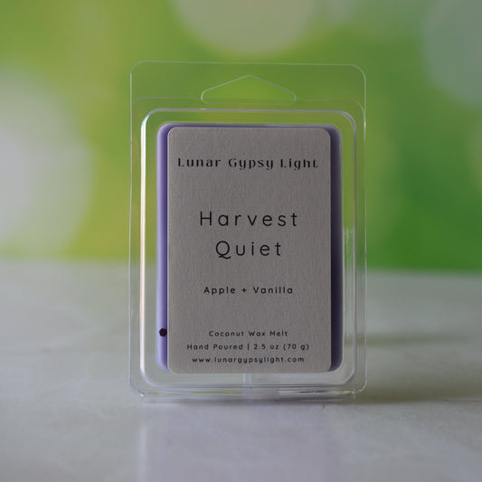 Packaged wax melt labeled Harvest Quiet on a white surface with green and yellow blurred background