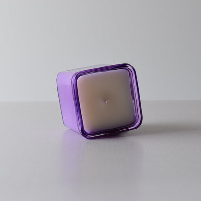 Square purple candle on a white surface with a light gray background