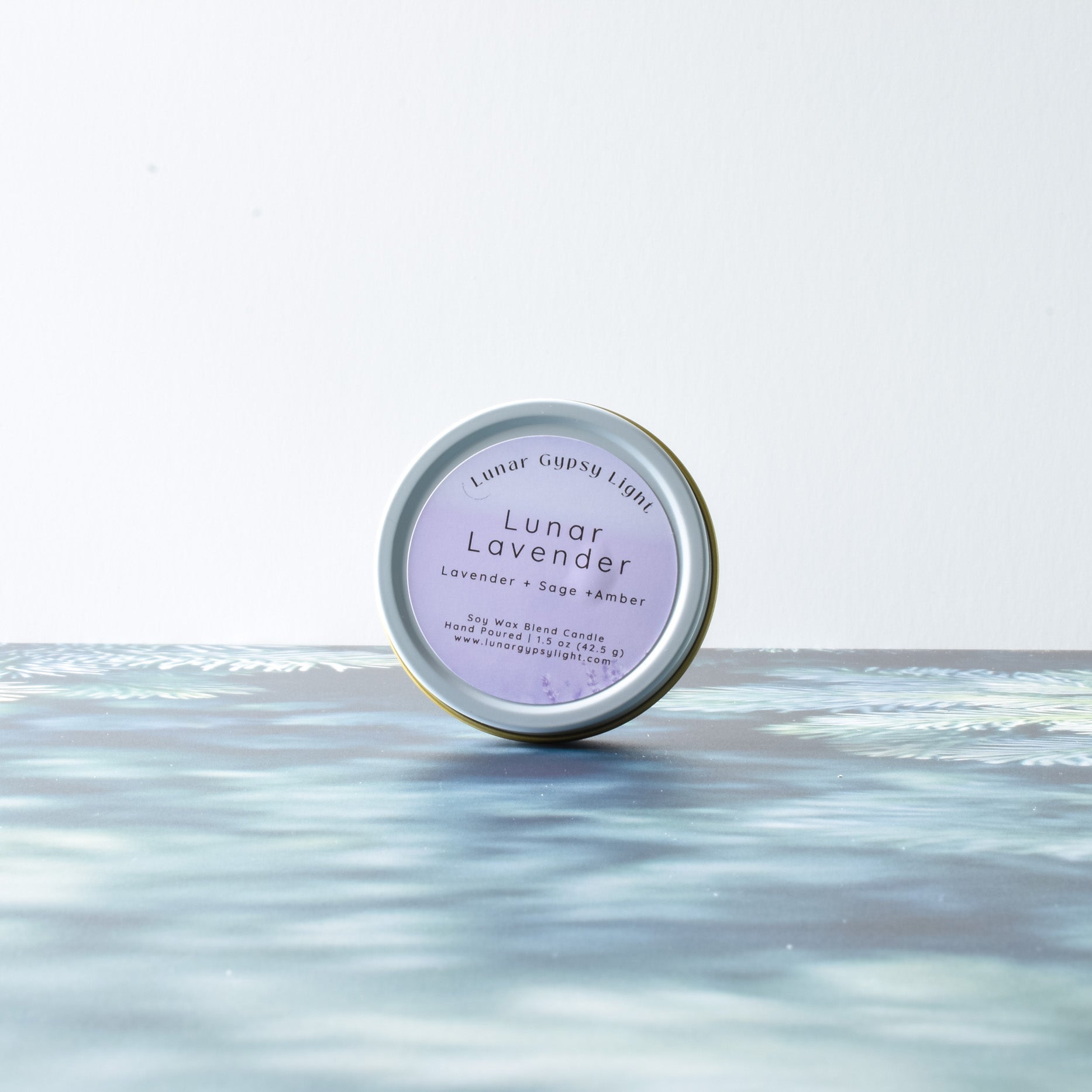 Lunar Lavender small candle tin product on a fir inspired surface with a white background