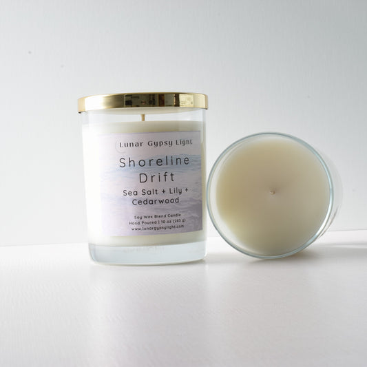 Candle with packaging labeled 'Shoreline Drift' on a white background and gold lid