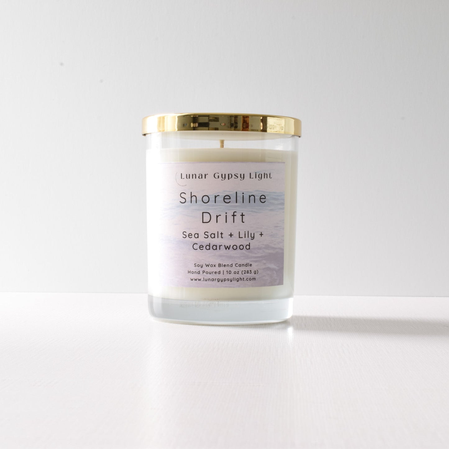Candle with a gold lid and label "Shoreline Drift" on a white background