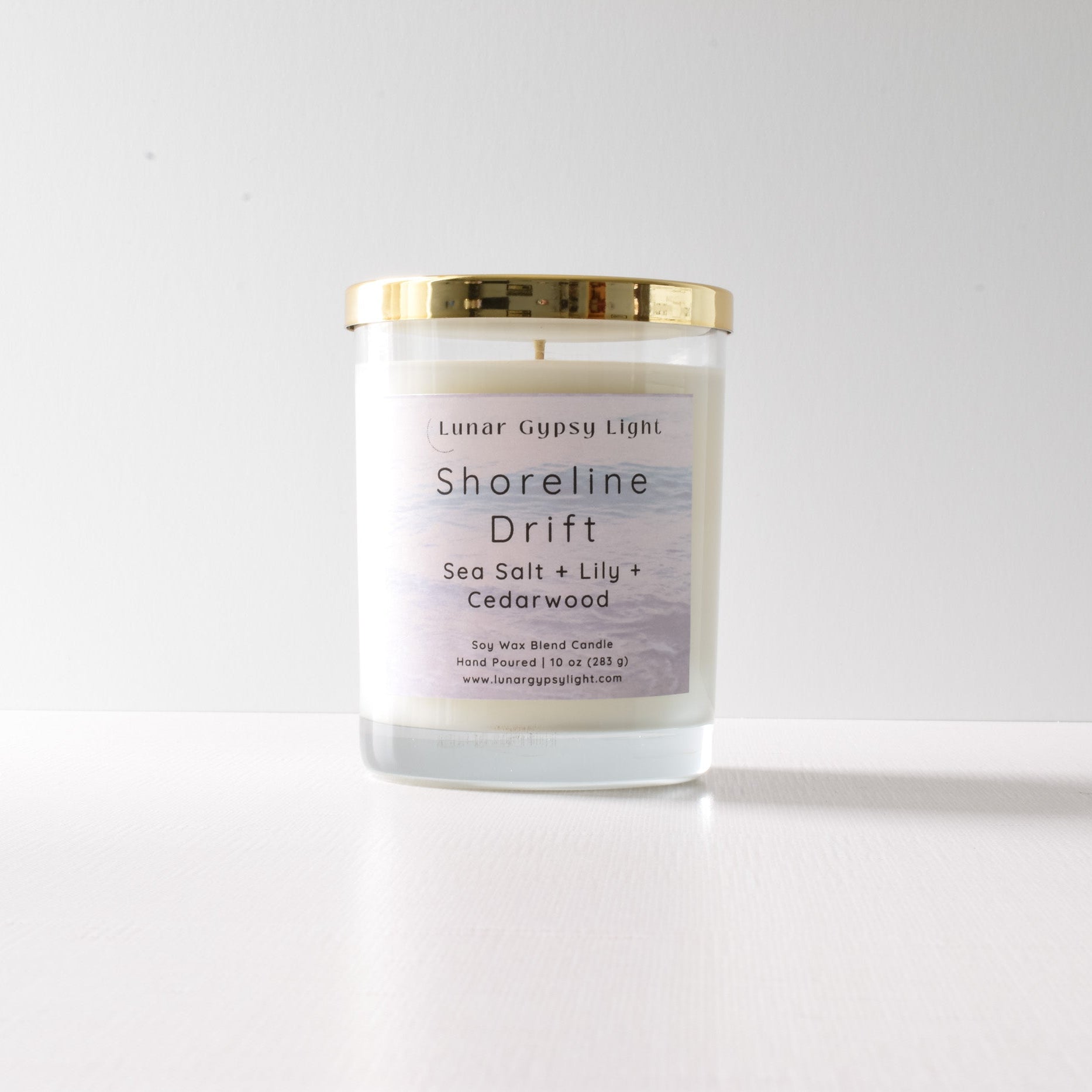 Candle with a gold lid and label "Shoreline Drift" on a white background