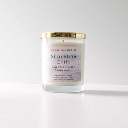 Candle with a gold lid and label "Shoreline Drift" on a white background
