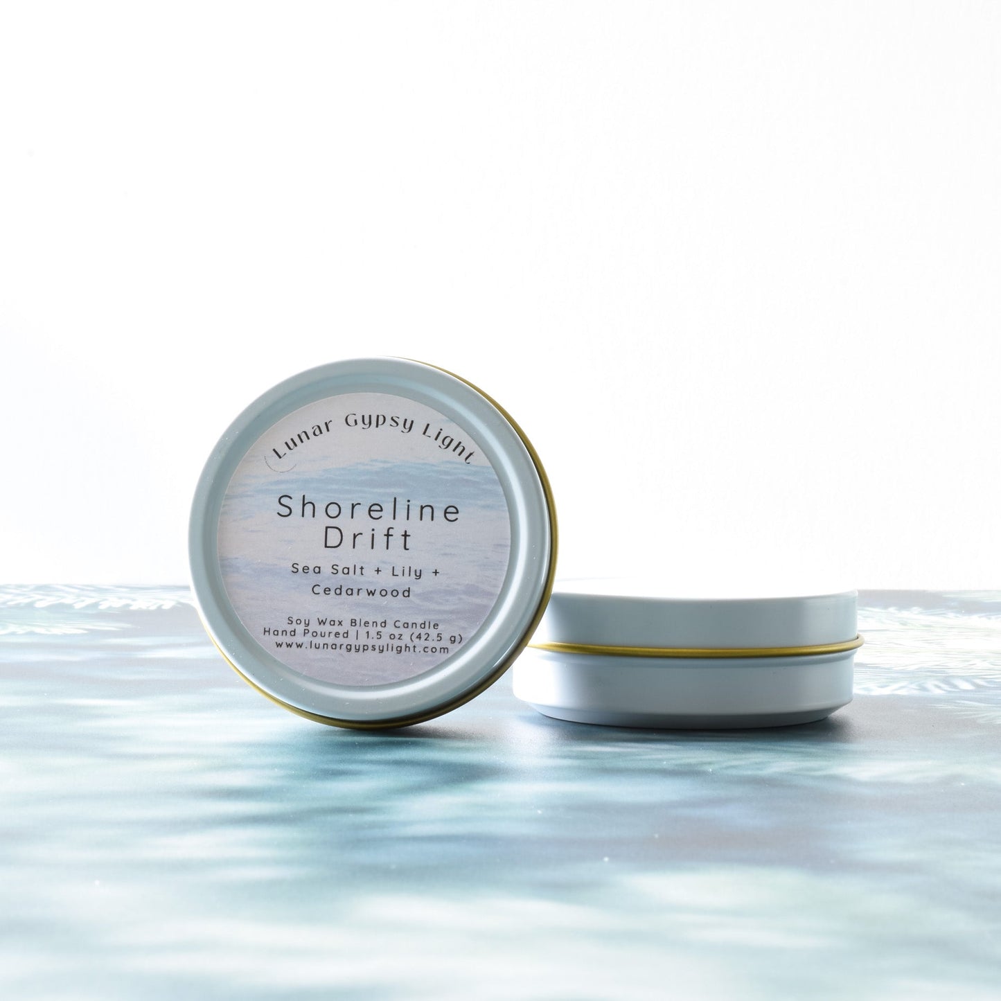 Candle tin Labeled 'Shoreline Drift' on a fir inspired surface with a white background
