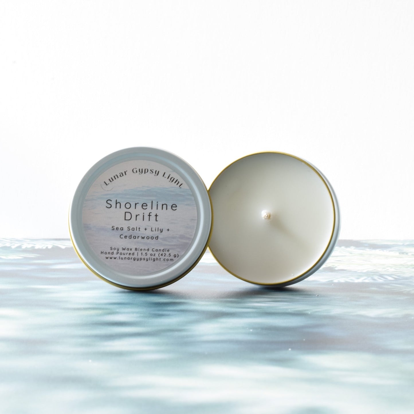 Small candle tin labeled Shoreline Drift on a fir inspired surface with a white background.